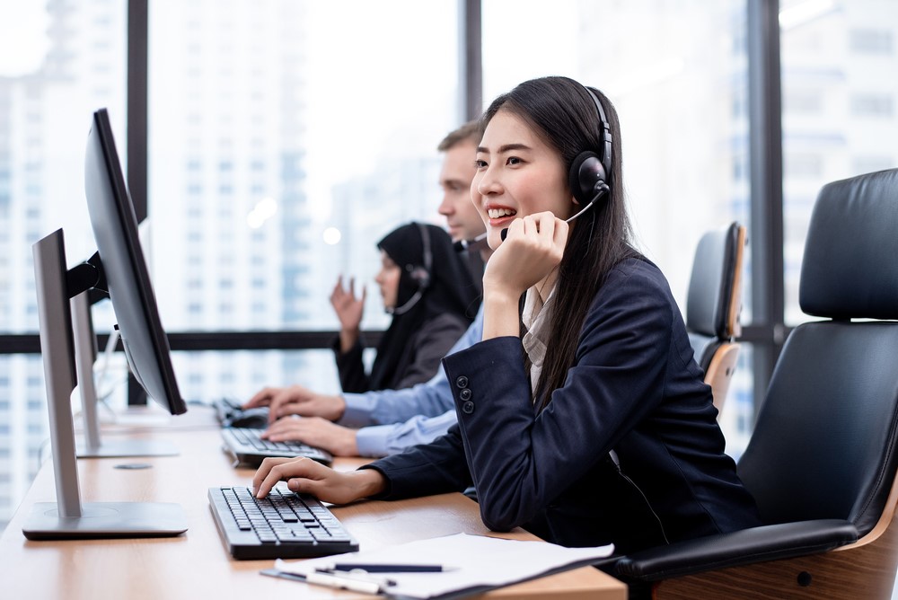 The Asian women call center is working in front of the computer with smiling face. Hot line operator support, customer relationship, service mind, 24 hours service, concept.